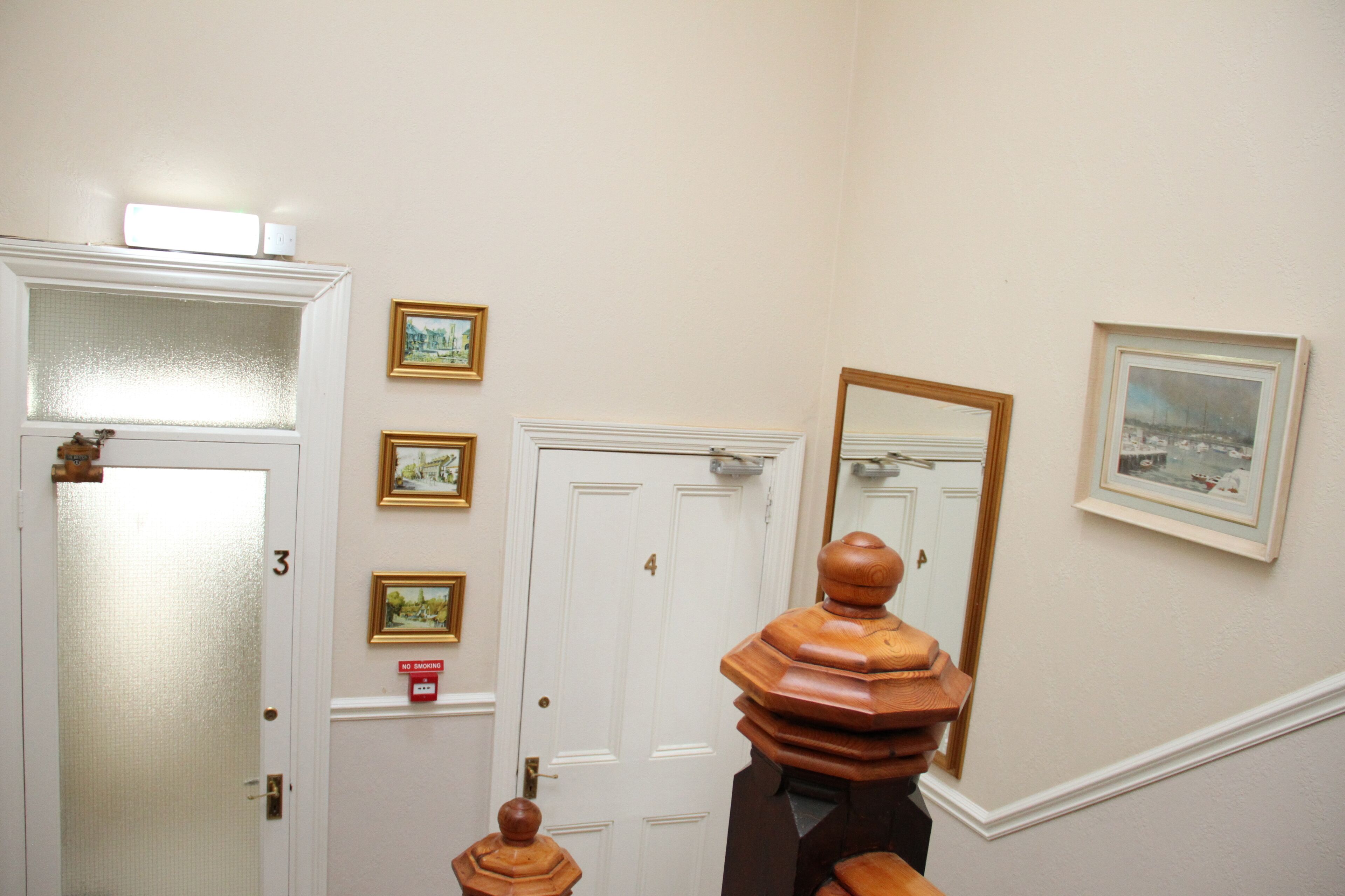 A hallway with a wooden handrail, a white door with a number, and framed pictures on the wall.