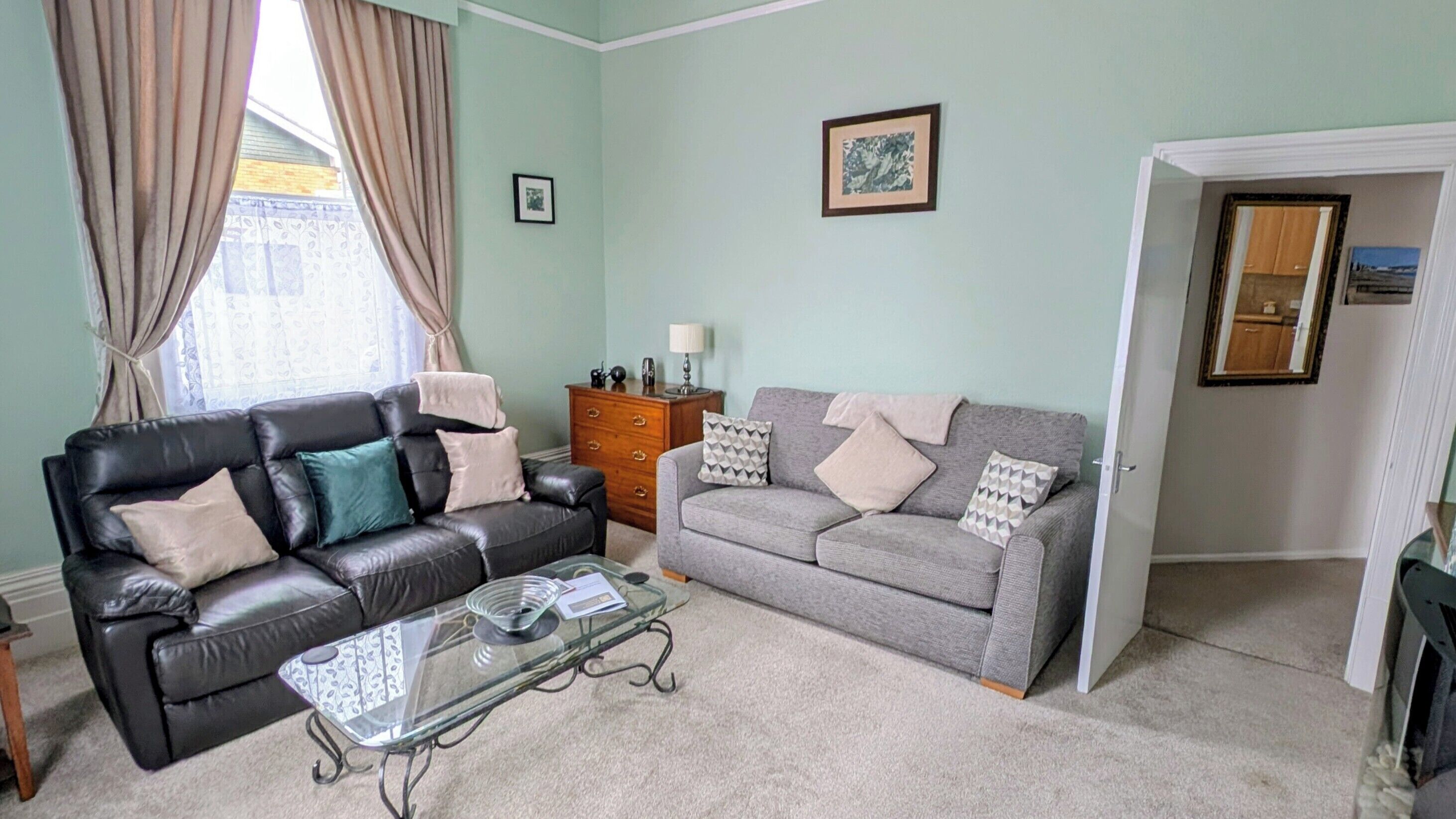 A living room with two sofas, a glass coffee table, a wooden side table, and a door leading to another room.
