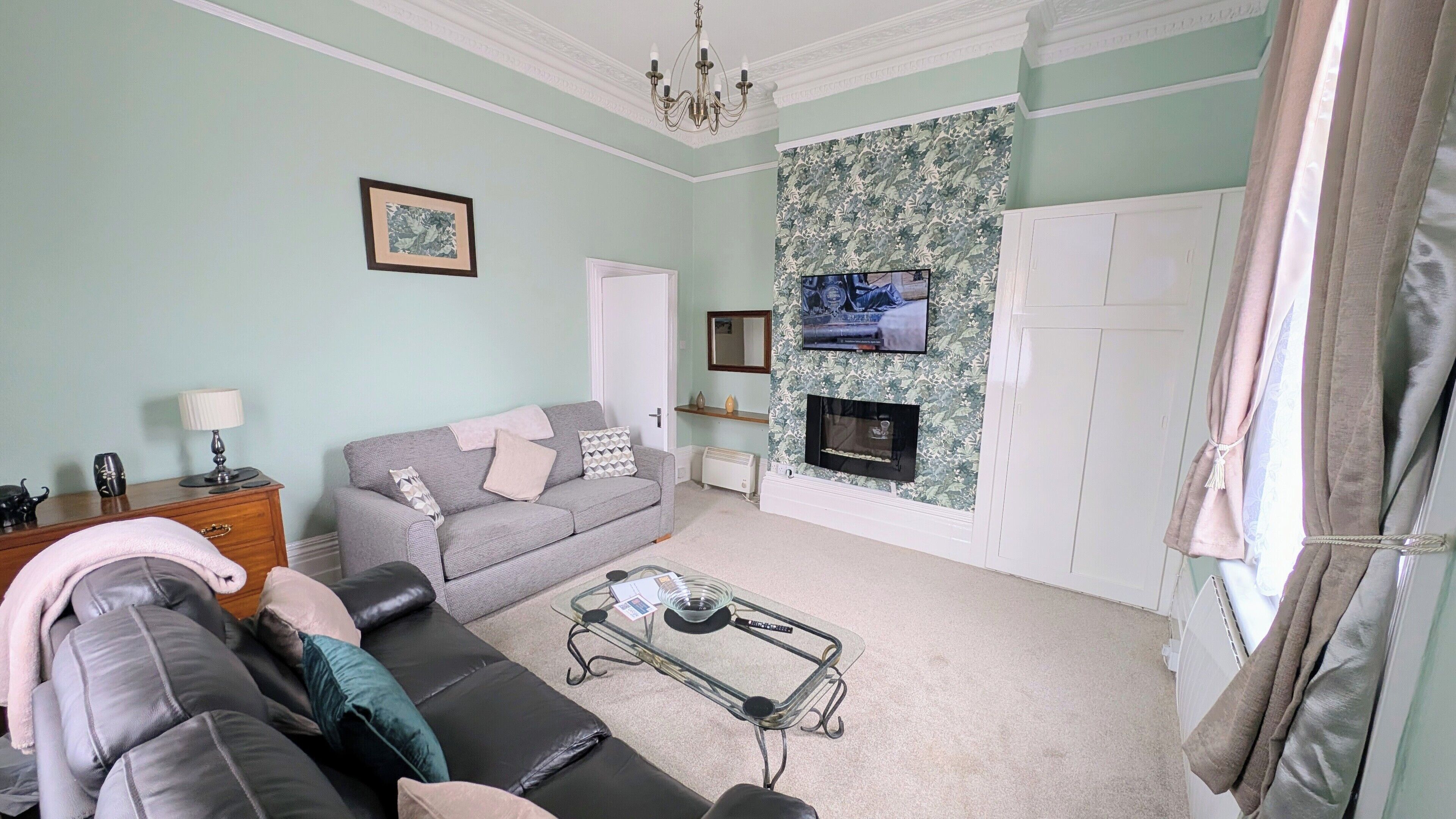Una sala de estar con sofá, una mesa de centro de vidrio, chimenea, televisor y pared con diseño.