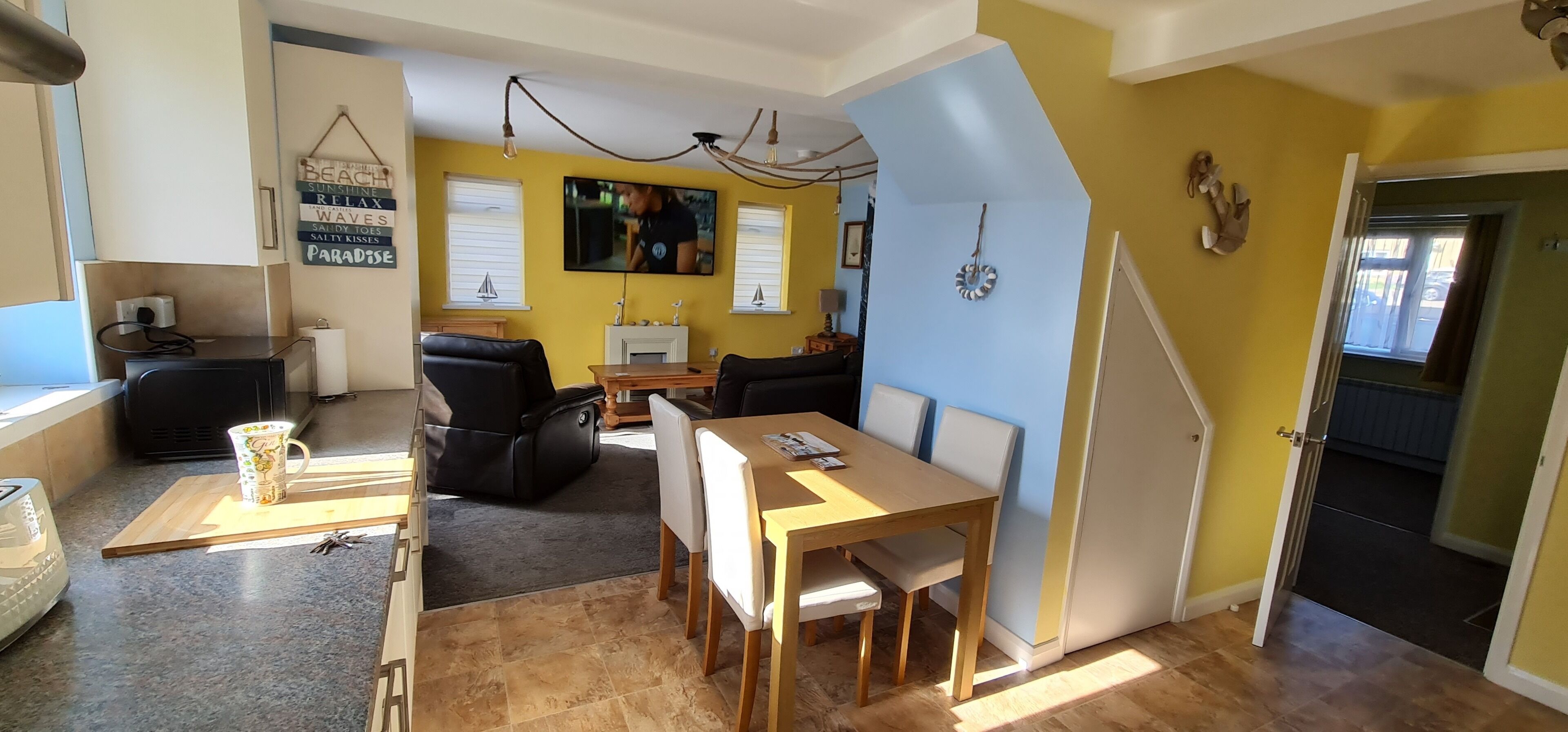 Un espace de vie compact comprenant un coin repas, une cuisine et un téléviseur fixé au mur.