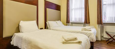 A hotel room with two beds, wooden headboards, and a window with curtains.