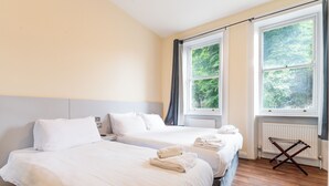 Una camera d'albergo con due letti, lenzuola bianche, un termosifone e una finestra con vista sugli alberi.