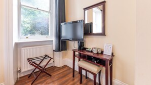 Una stanza con televisione, un tavolino con un cartello, un termosifone e una finestra con tende.