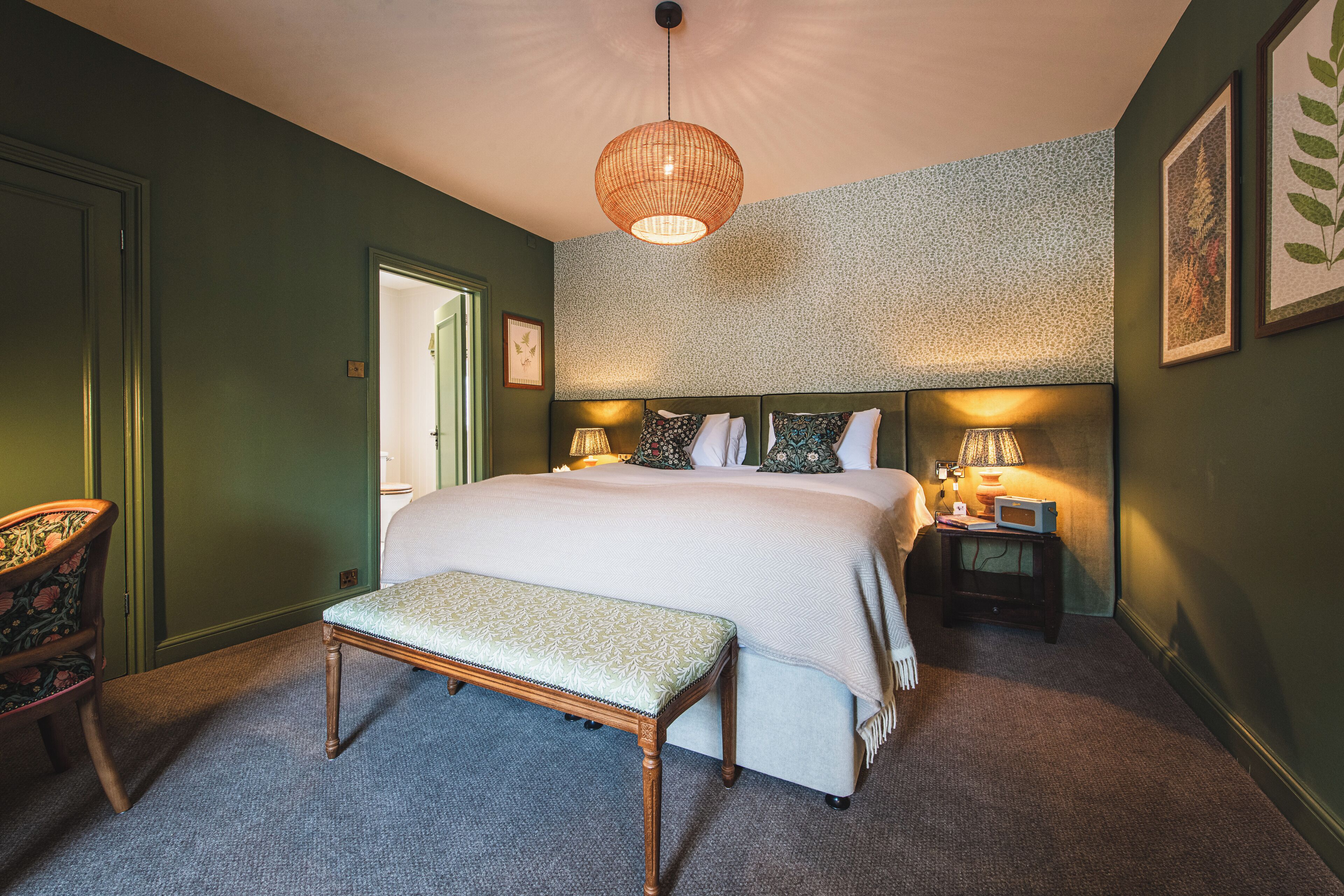 A bedroom with a large bed, a bench, a nightstand with a lamp, and a chair.