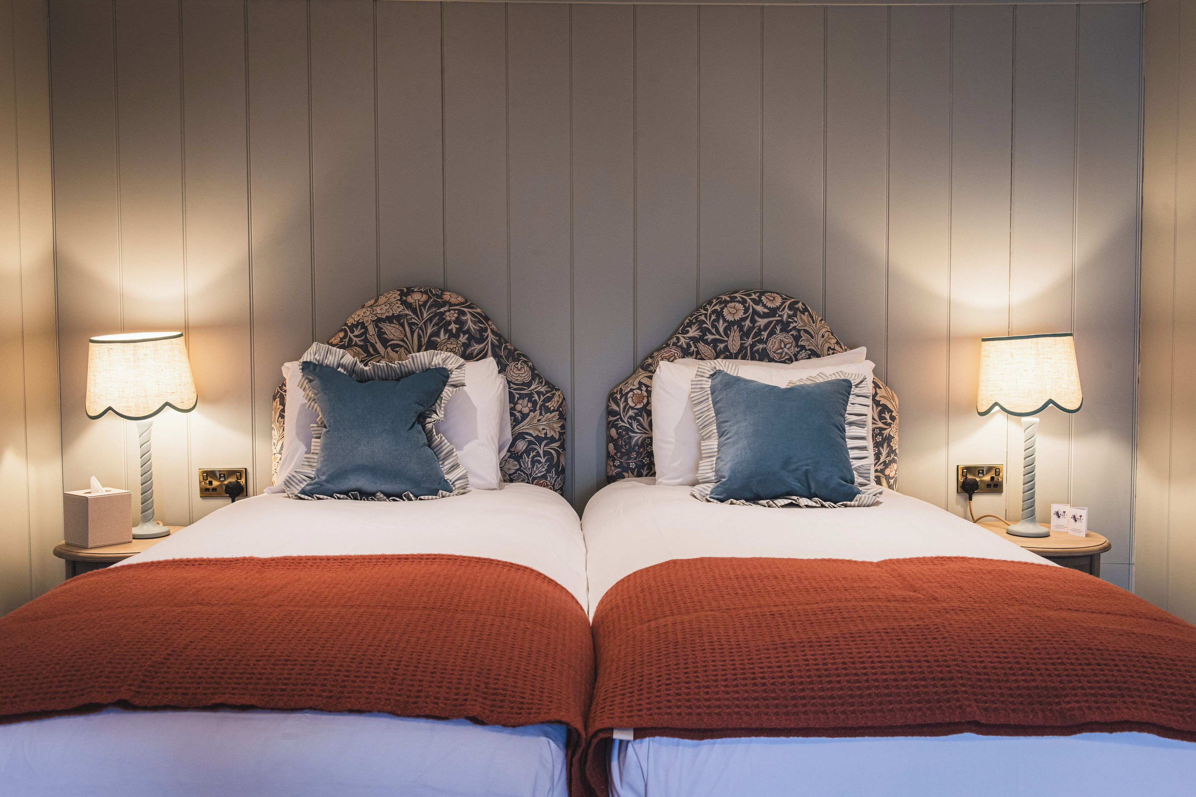 A double bed with a red blanket, two nightstands with lamps, and patterned headboards.