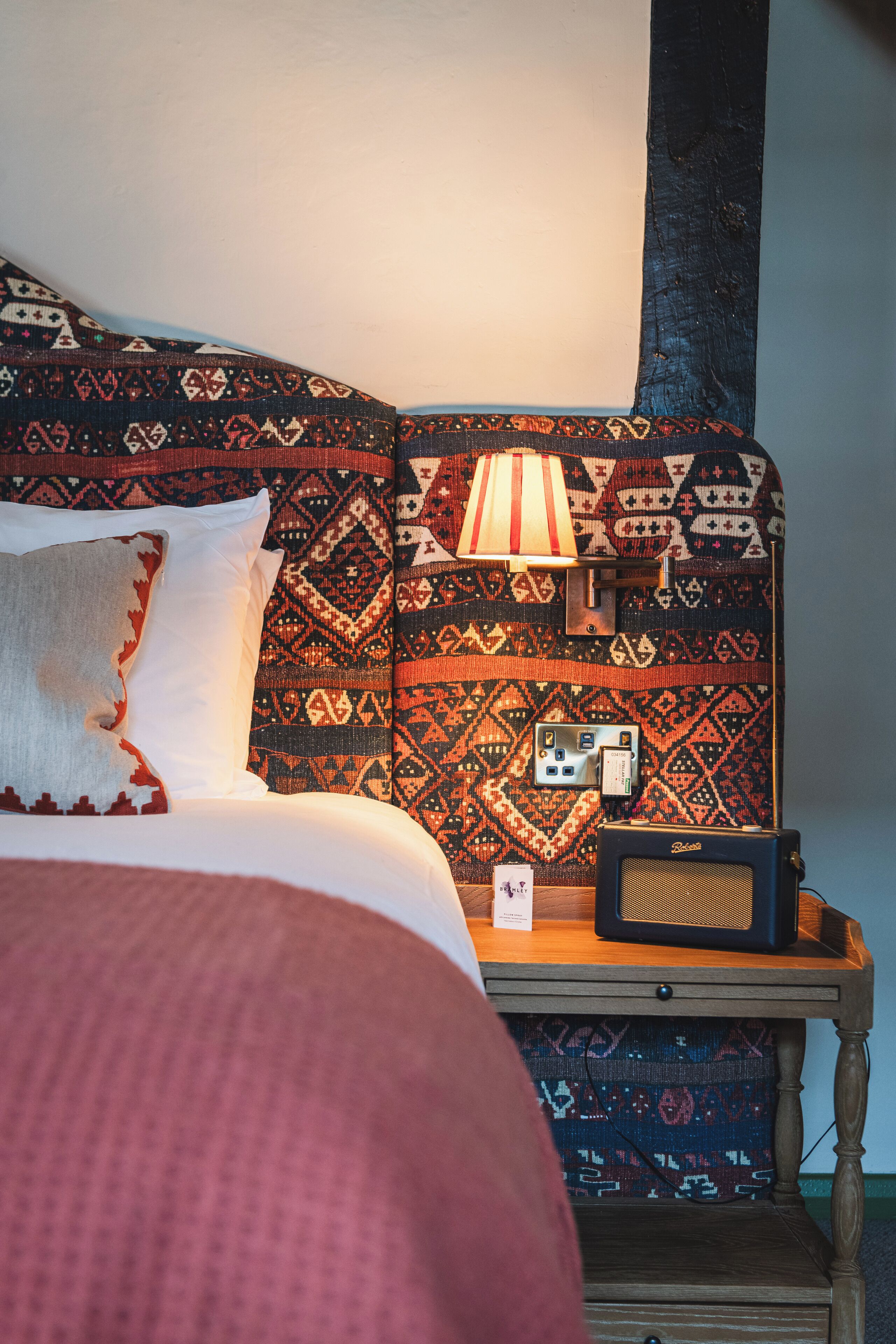 A bed with patterned bedding, a bedside lamp, and a radio on a wooden nightstand.
