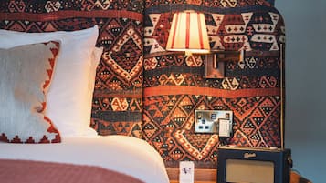 A bed with patterned bedding, a bedside lamp, and a radio on a wooden nightstand.
