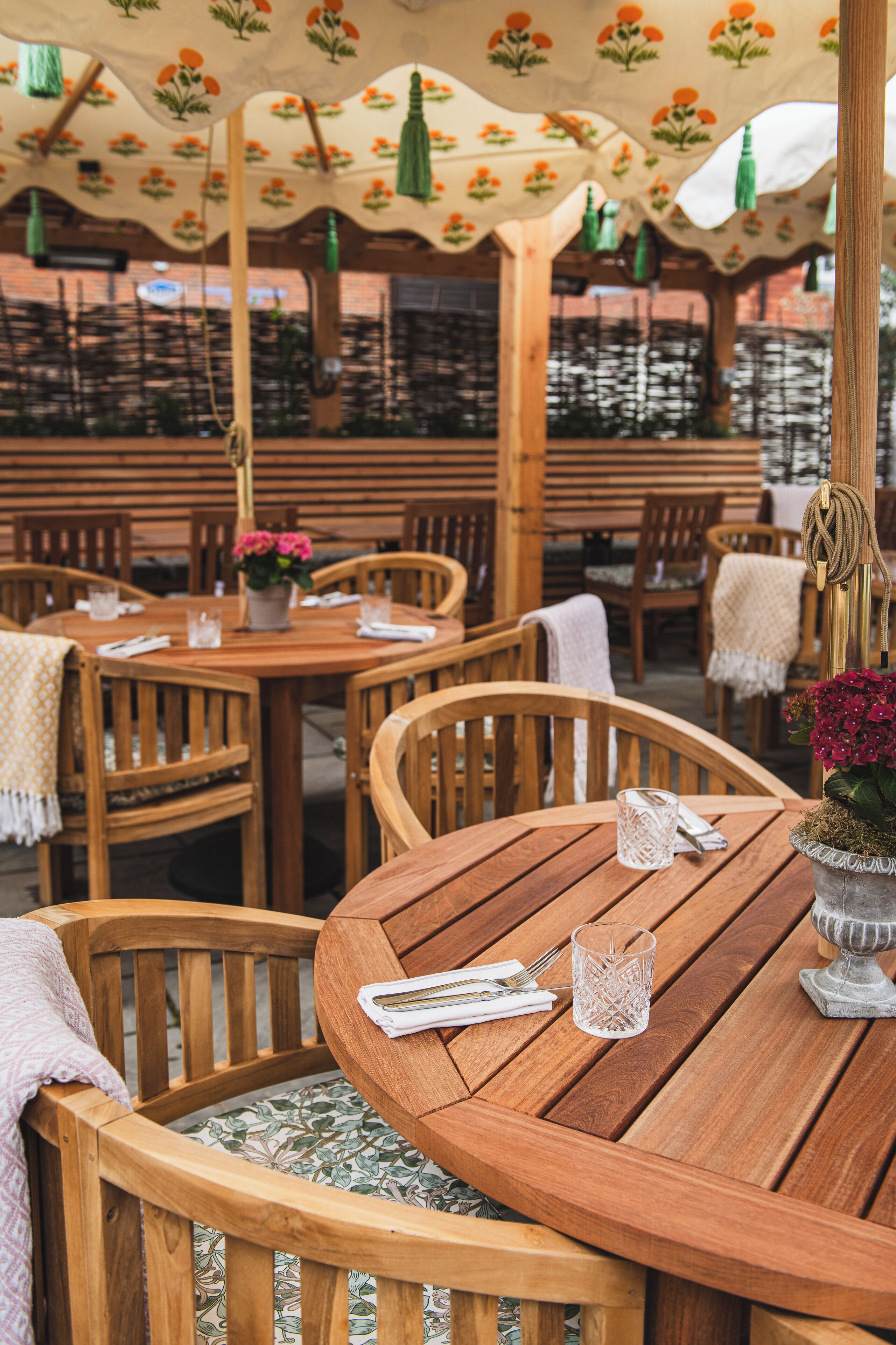 A wooden outdoor dining area with tables and chairs, covered by patterned umbrellas.