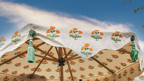 Un área de estar al aire libre con mesas y sillas de madera, cubierta por sombrillas con estampados florales.