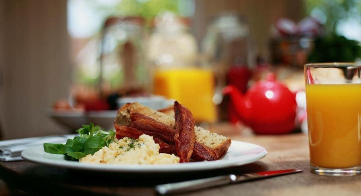 A breakfast setting with scrambled eggs, bacon, toast, and a glass of orange juice on a table.