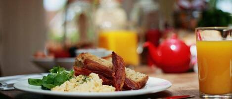 Un desayuno con huevos revueltos, tocino, tostadas y un vaso de jugo de naranja en una mesa.