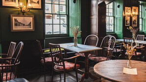 Interior de un pub tradicional con mobiliario de madera, cuadros enmarcados en las paredes y amplias ventanas.