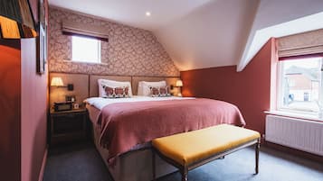 Um quarto com cama, luminárias de cabeceira, um banco, uma janela e um radiador.