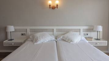 Un llit doble amb llençols blancs, dues taules de nit amb làmpades i una làmpada penjant a la paret.