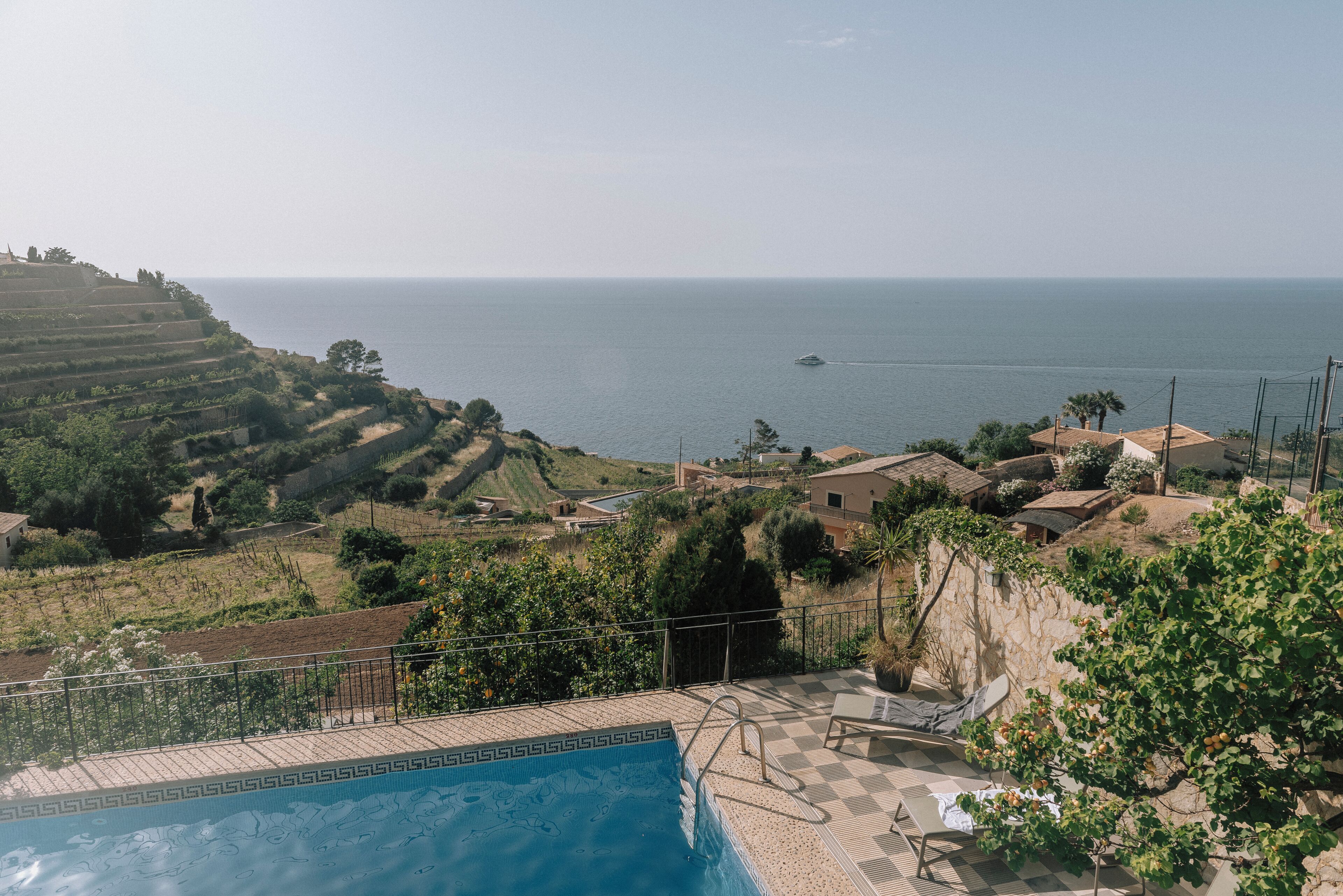 A pool with a view of the sea and terraced fields.