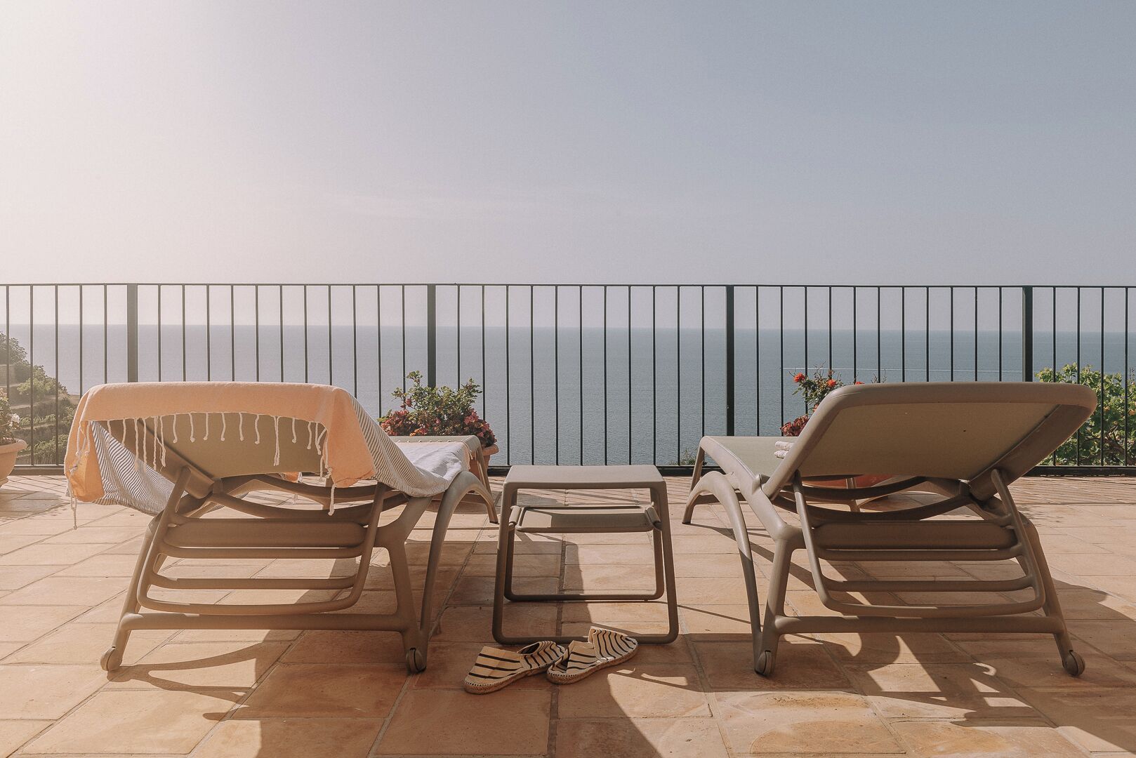 A terrace with two lounge chairs, a small table, and a pair of slippers on the floor.