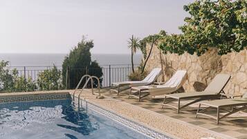 Zona de piscina con sillones y vista al mar.