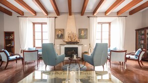 Una sala de estar con dos sillones azules, una mesa de centro de vidrio con una vela, una chimenea y un modelo de barco sobre la repisa.