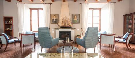 A living room with two blue armchairs, a glass coffee table with a candle, a fireplace, and a ship model on the mantel.