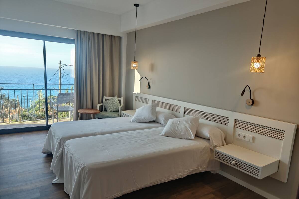 Un dormitorio con dos camas, una silla, una mesita y vista al mar.