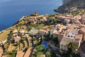 An aerial view of a coastal town with buildings, a swimming pool, and a view of the sea. - Hostal Sa Baronia (Banyalbufar)