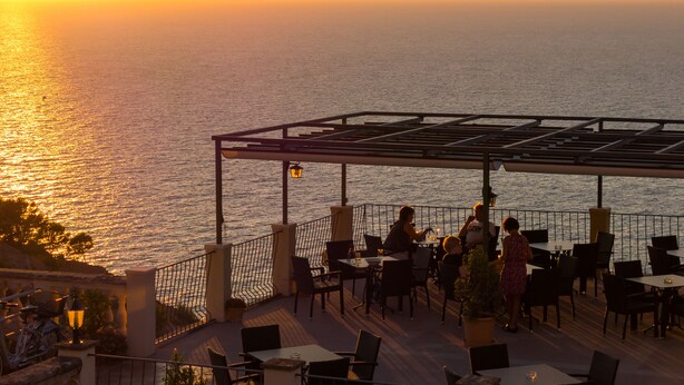 Una terraza con mesas y sillas que da al mar al atardecer.