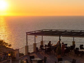 Una terraza con mesas y sillas que da al mar al atardecer.
