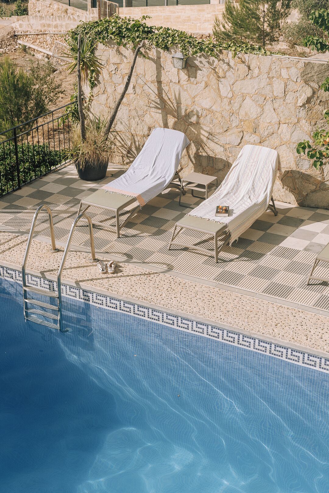 Un área de piscina con dos tumbonas, un muro de piedra y una planta en maceta.