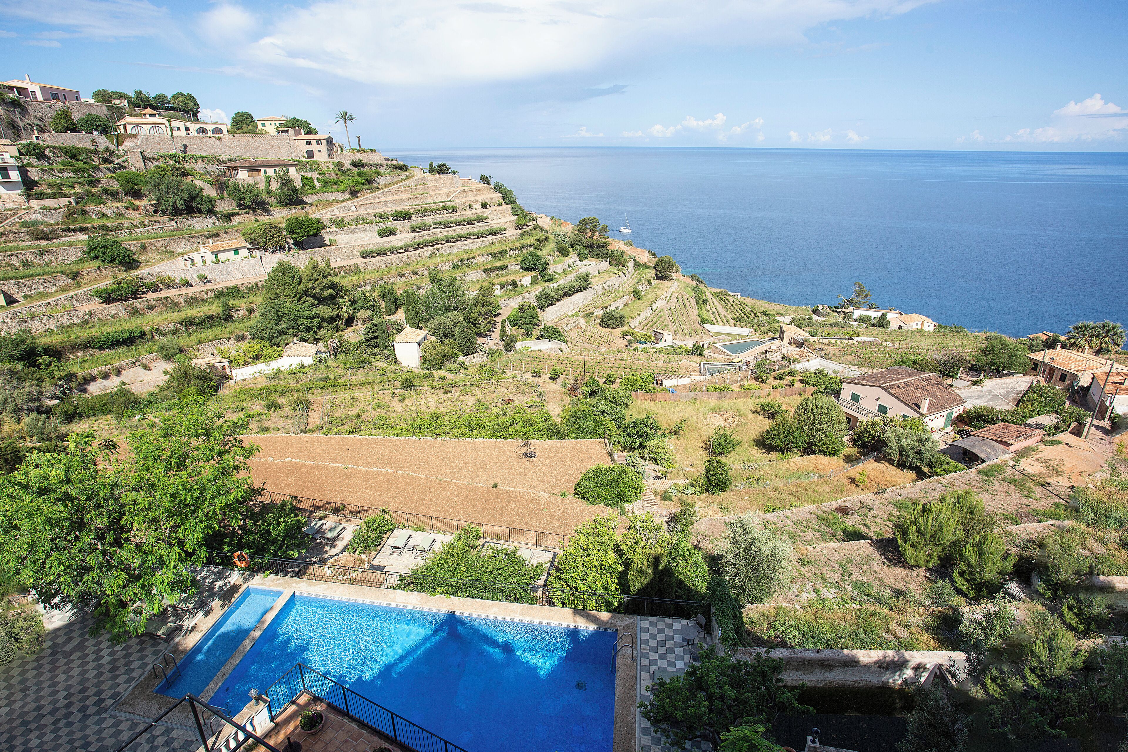 A hillside property with a swimming pool, terraced gardens, and a view of the sea.