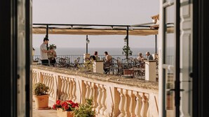 Un umbral abierto que da a una terraza con mobiliario exterior, plantas en macetas y vistas al mar.