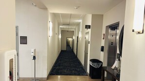 A hotel hallway with a carpeted floor, a trash bin, a hand sanitizer dispenser, and an elevator. - Comfort Suites Plymouth near US-30 (Plymouth)