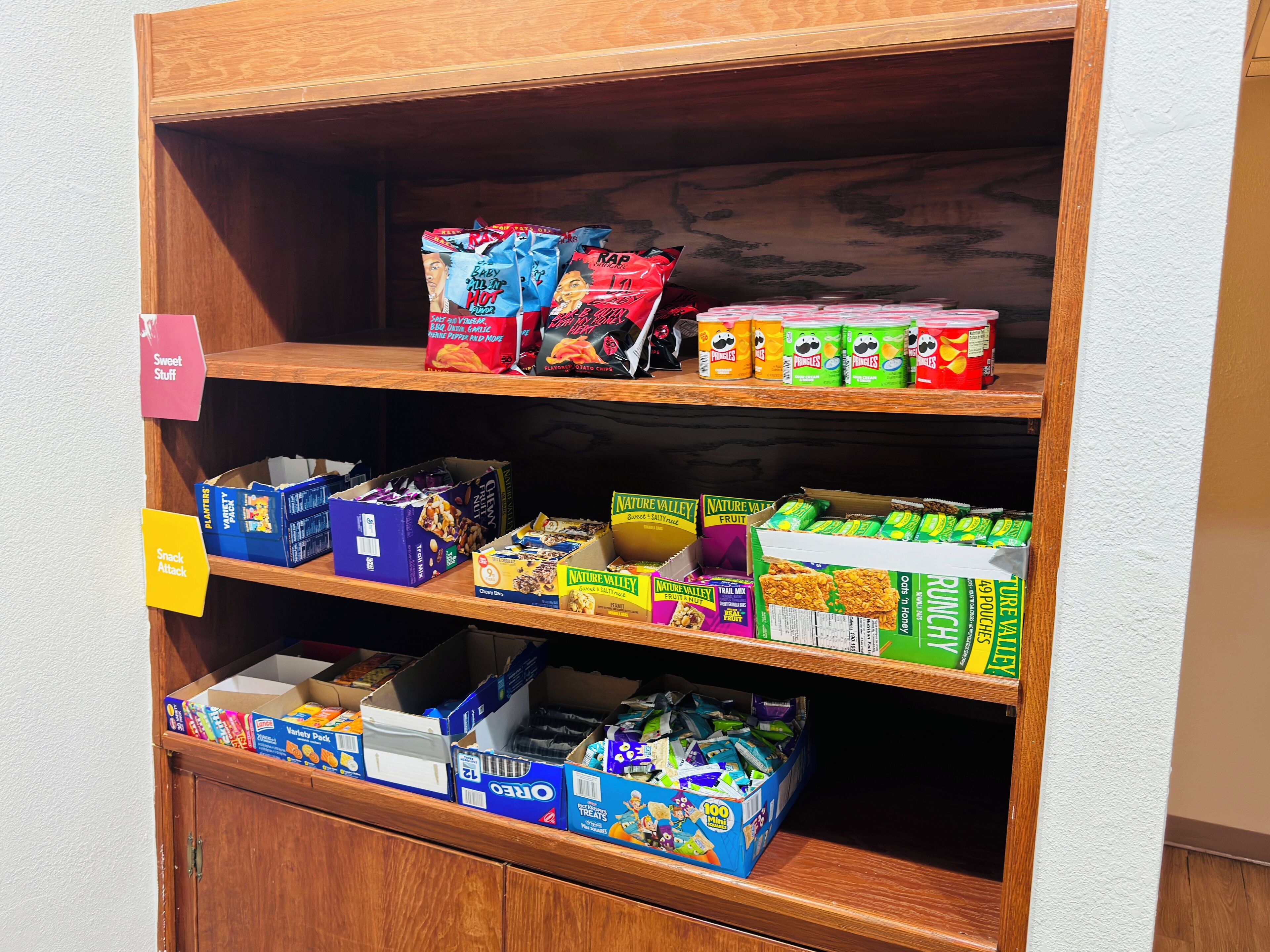 A shelf stocked with various snack and food items, including chips, cereal, and other packaged goods.