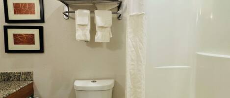 A bathroom with a toilet, a shower curtain, and a towel rack with towels.