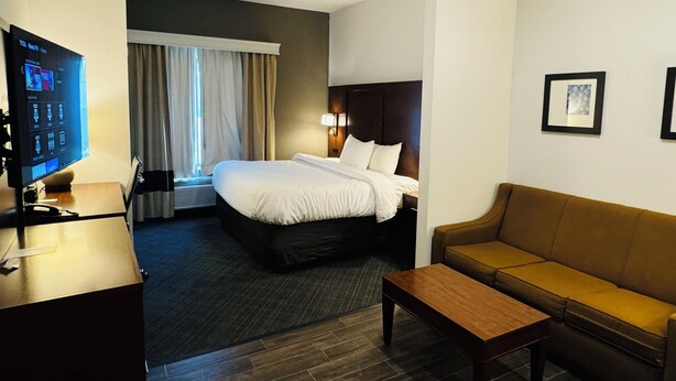 A hotel room with a bed, a desk with a computer, a sofa, and a window with curtains. - Comfort Suites Plymouth near US-30 (Plymouth)