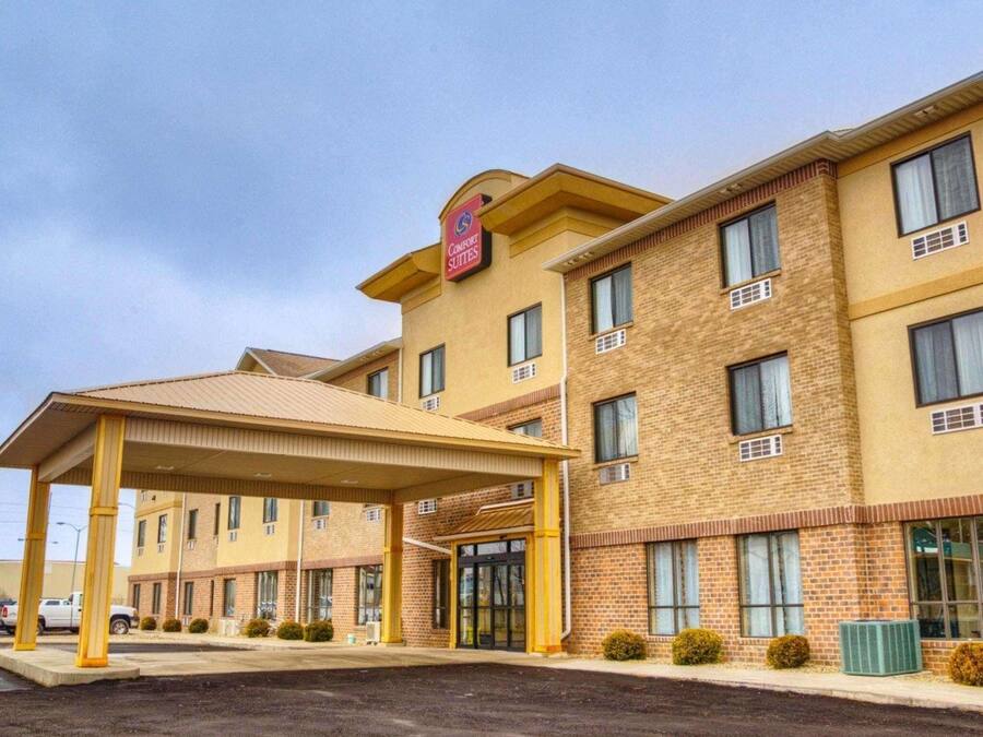 Een hotel met een overdekte ingang, meerdere ramen en een bordje met de tekst 'Comfort Suites'.