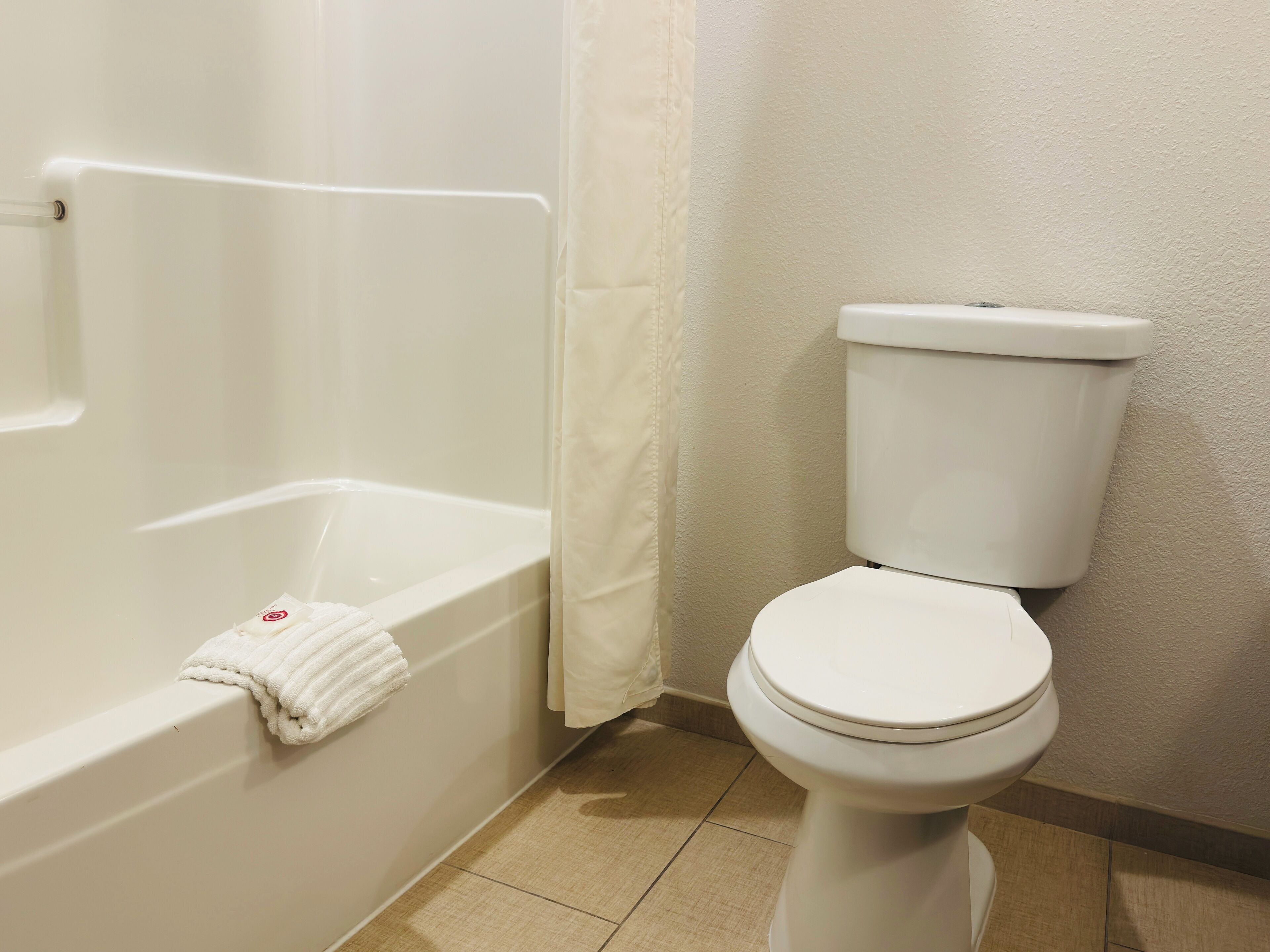 A bathroom with a white bathtub, a white toilet, and a beige tiled floor.