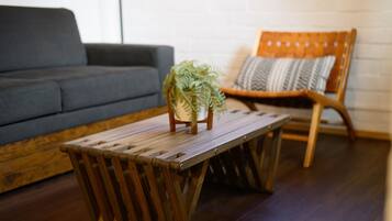A wooden coffee table with a potted fern, a grey sofa, and a wooden chair with a cushion.