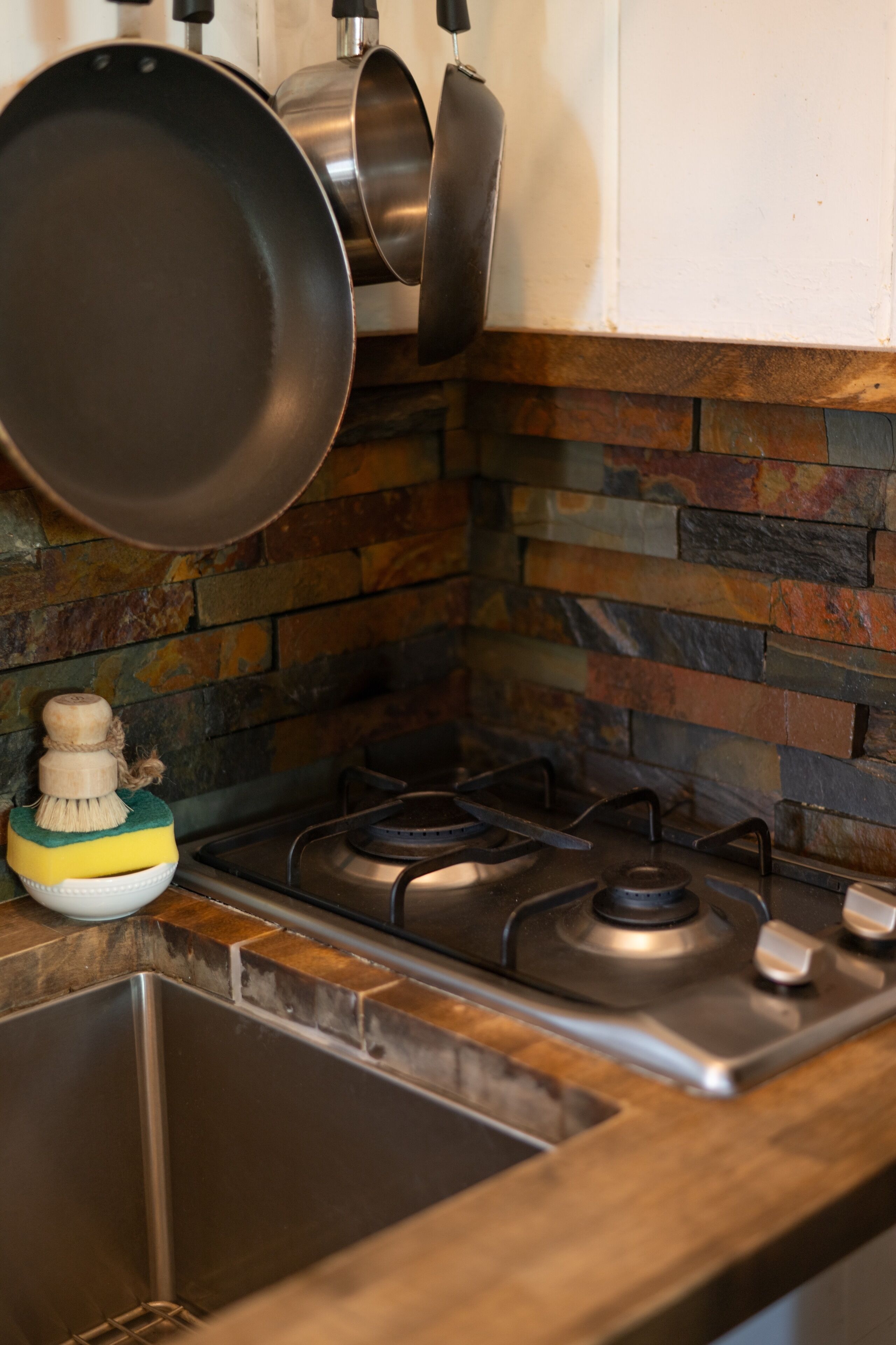 A kitchen with a gas stove, a sink, and a stone backsplash.