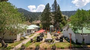A courtyard with outdoor seating, a large tree, and a mountain backdrop. - Lake Front Cabins (June Lake)