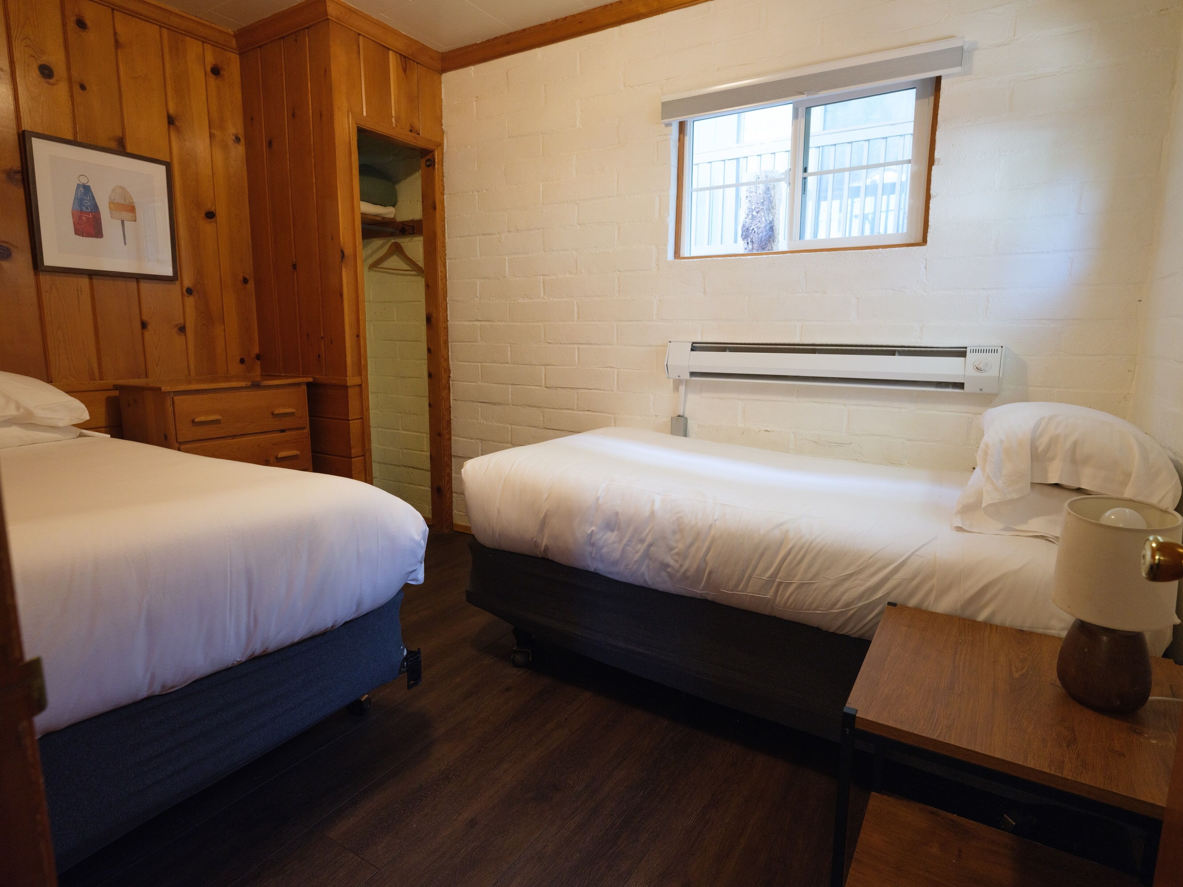 Habitación con dos camas, armario de madera, paredes de ladrillo blanco y una ventana con persianas.
