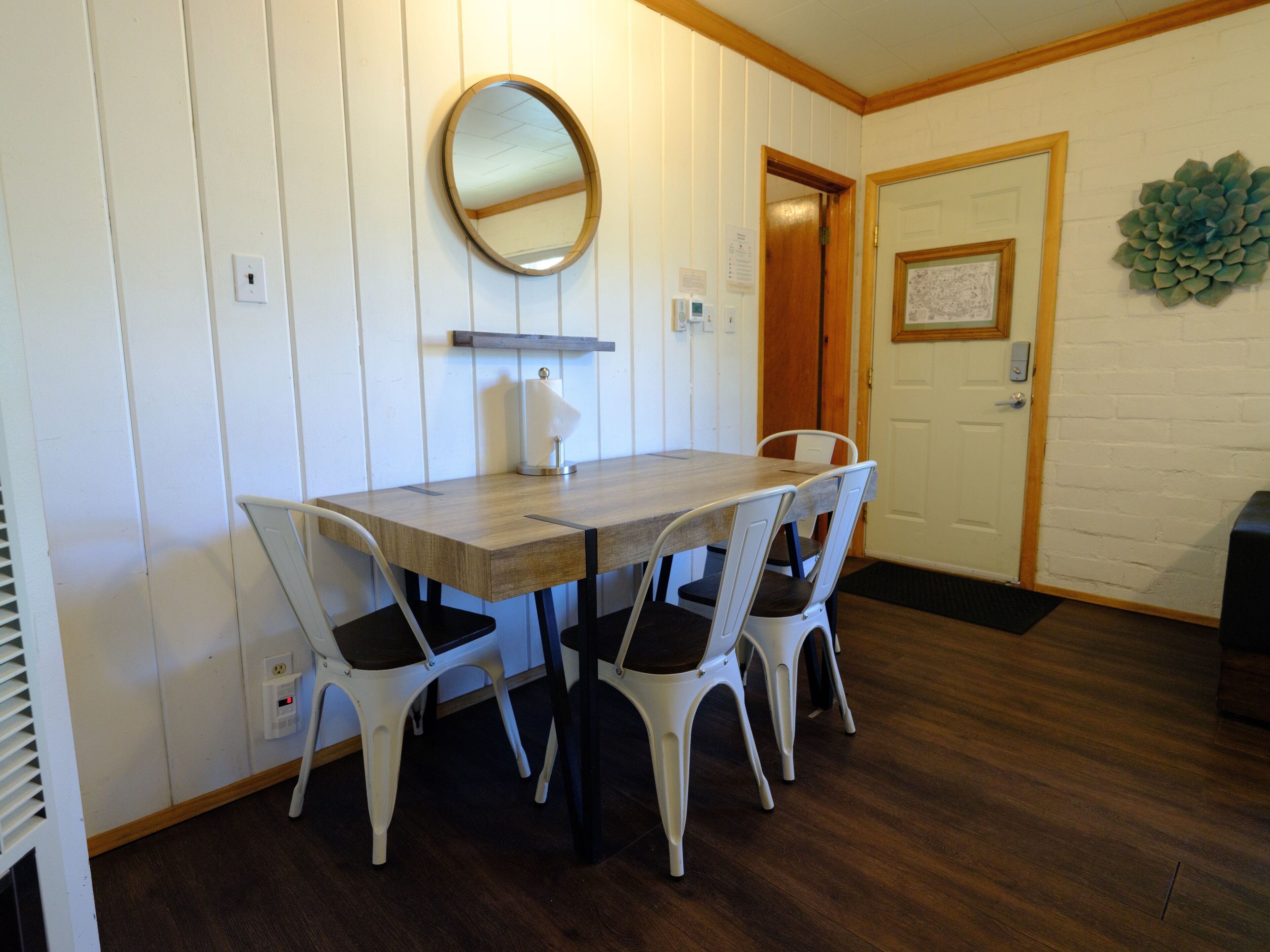 Un'area pranzo con tavolo in legno e sedie bianche, uno specchio a parete e una porta decorata con un elemento verde.