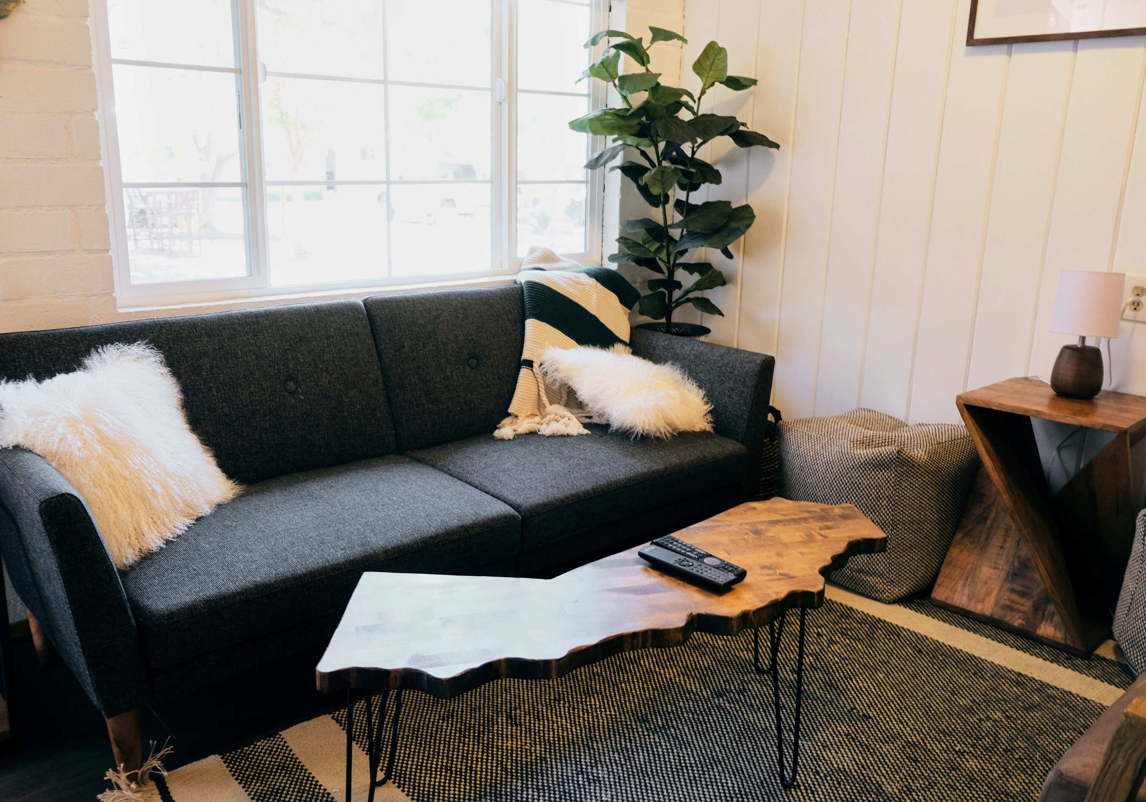 Una sala de estar moderna con un sofá gris, una mesa de centro de madera y una planta en maceta.