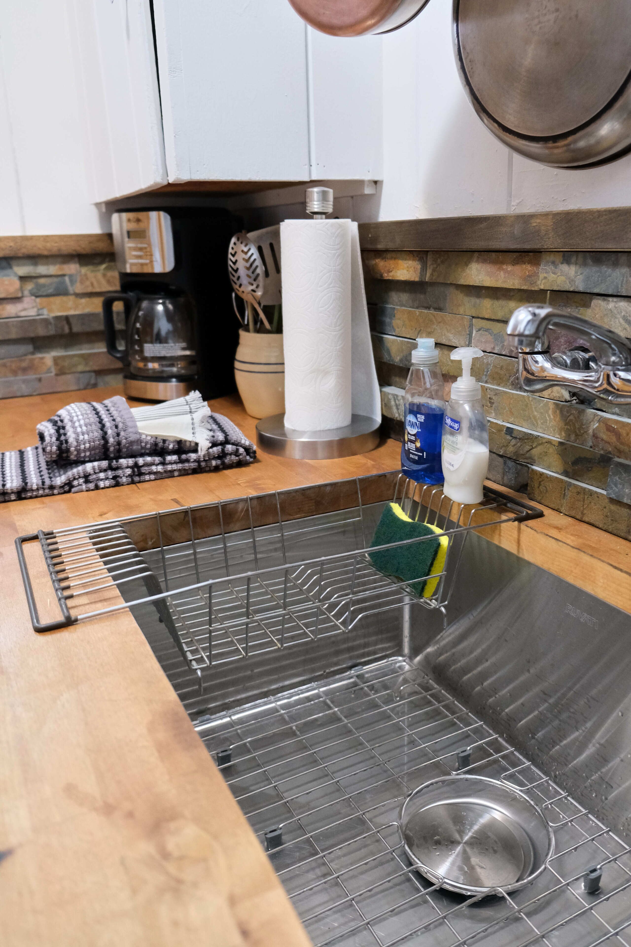 A kitchen with a stainless steel sink, a drying rack, and cleaning supplies.