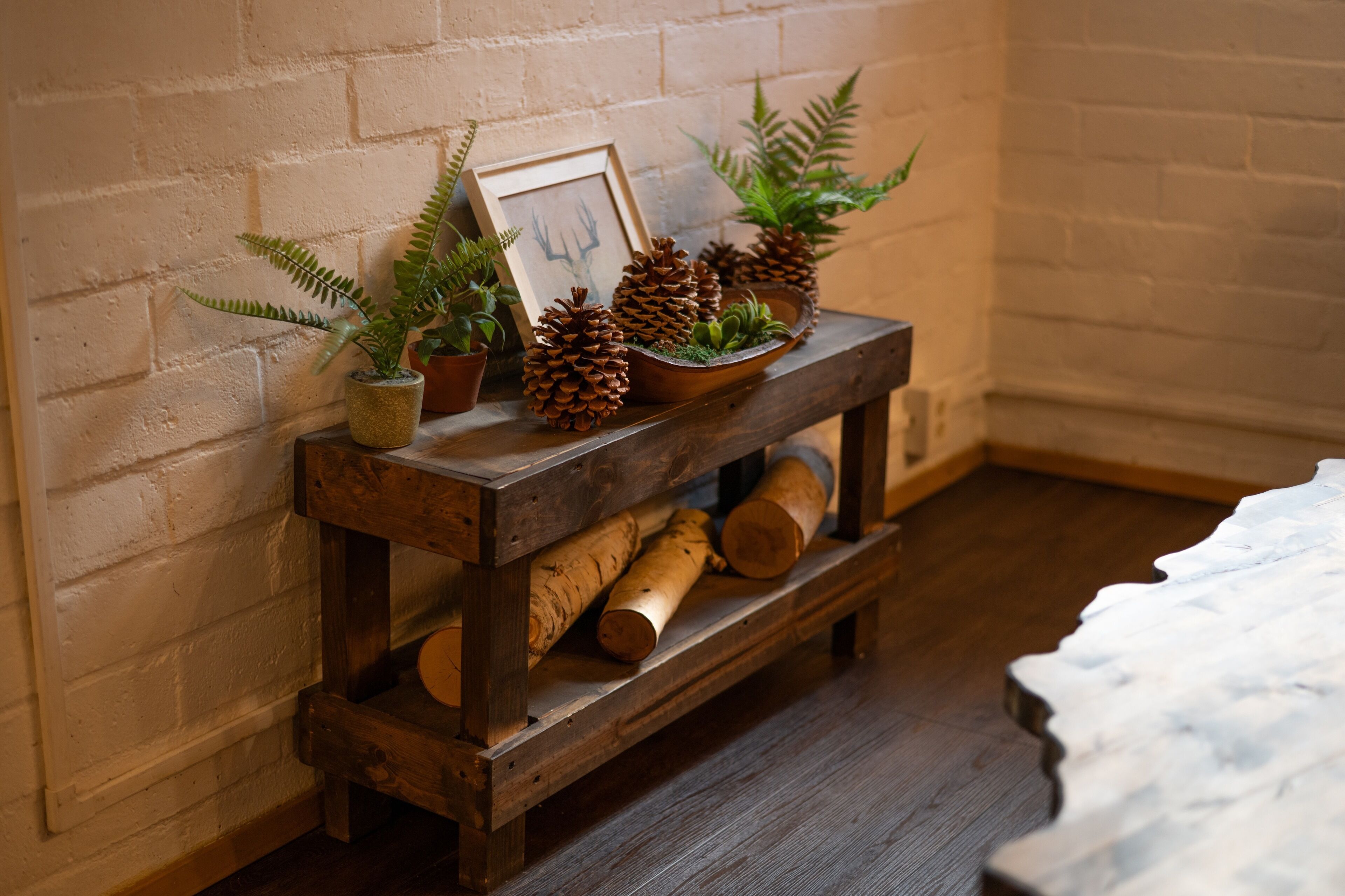 A rustic wooden bench with pinecones, ferns, and a framed picture against a brick wall.