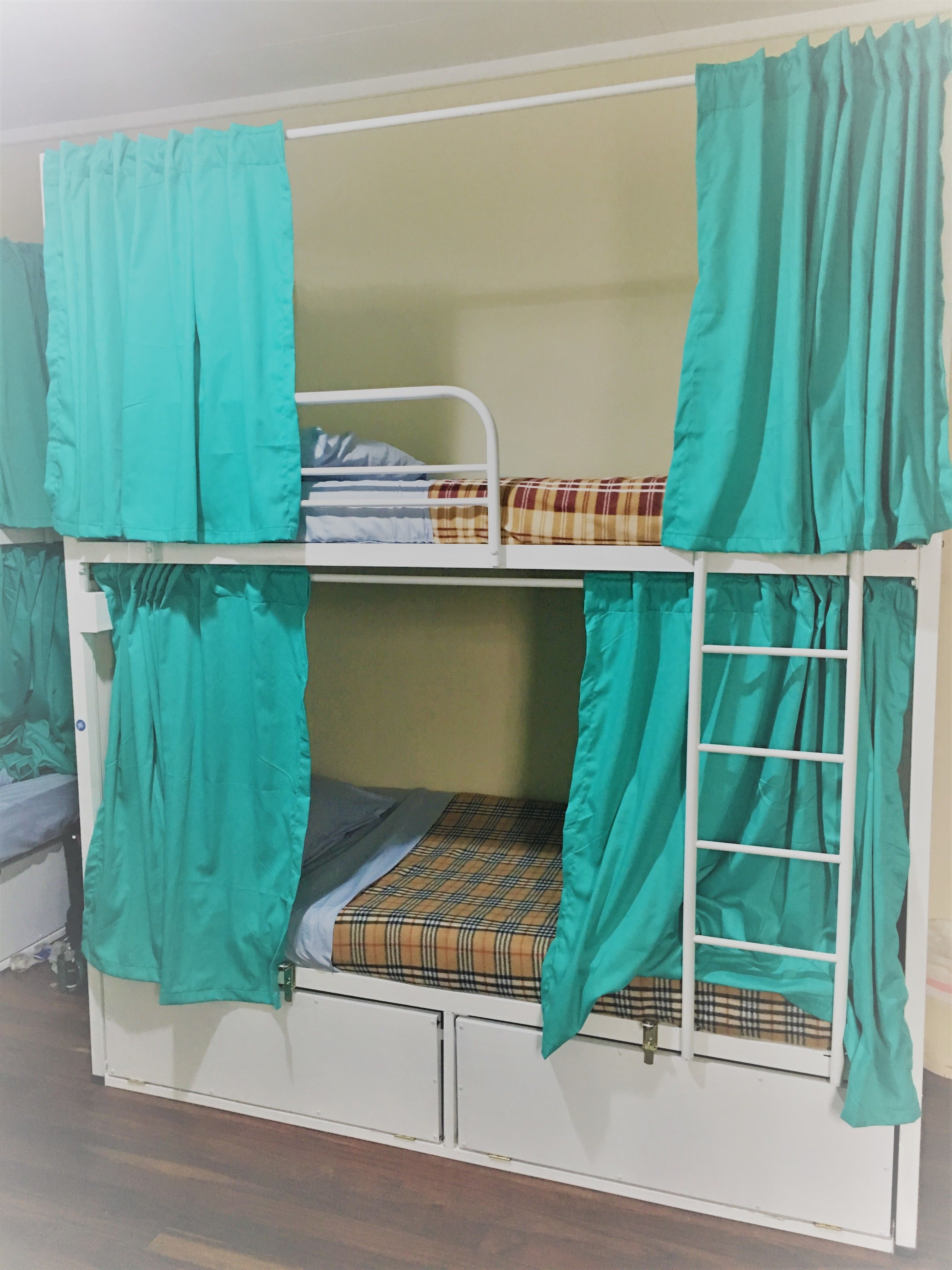 A bunk bed with teal curtains, a plaid mattress, and a ladder.