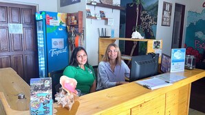 A reception desk with a wooden counter, a blue refrigerator, and various items on shelves behind the counter. - Costa Rica Backpackers - Hostel (San José)