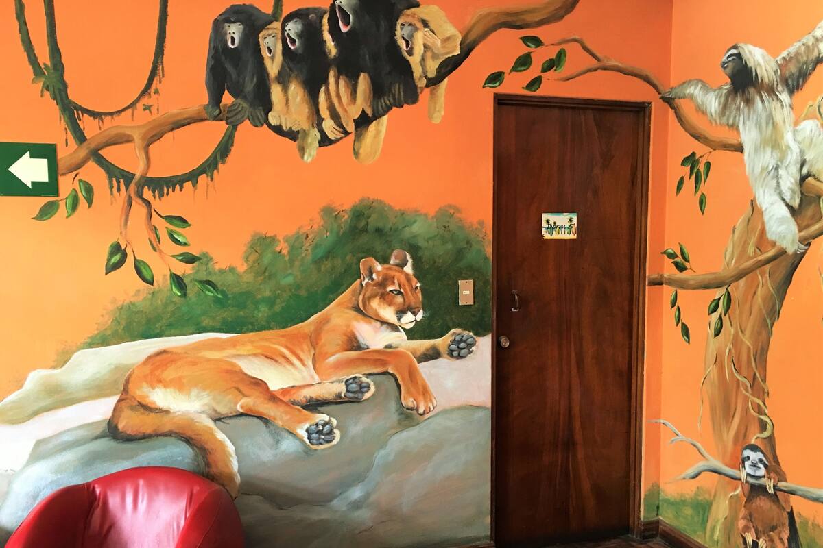 A room with a mural of a lion, monkeys, and a sloth. There is a red chair and a wooden door with a sign above it.