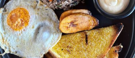 Un plato con arroz frito, un huevo frito, plátanos fritos y un recipiente pequeño con salsa.