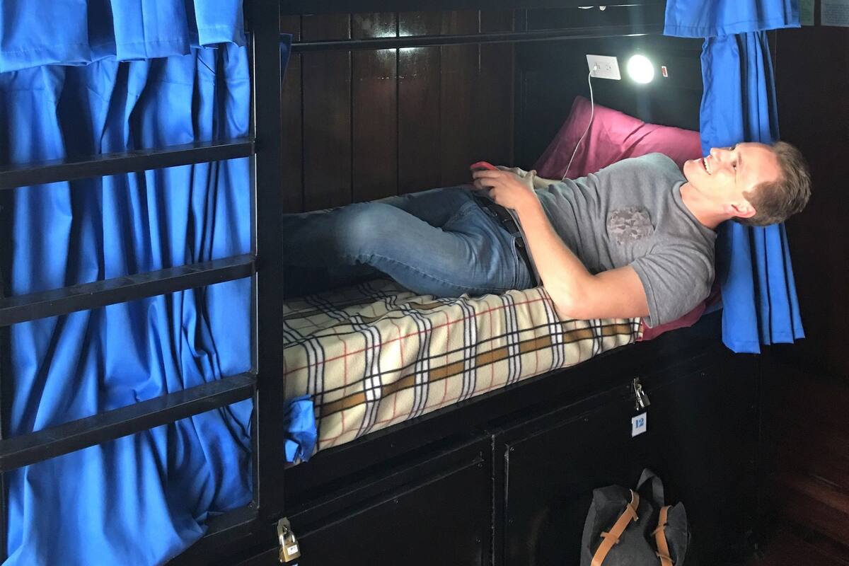 A bunk bed room with blue curtains, a mattress with a plaid pattern, and a black metal frame.