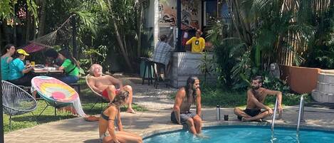 A poolside area with people relaxing and a covered structure in the background.
